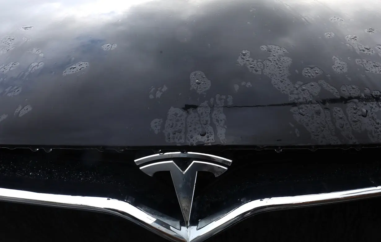 The logo of a Tesla electric vehicle is placed on a car outside a dealership in Drogenbos