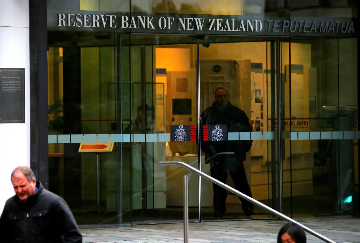FILE PHOTO: Pedestrians walk past as a security guard stands in the main entrance to the Reserve Bank of New Zealand located in central Wellington, New Zealand