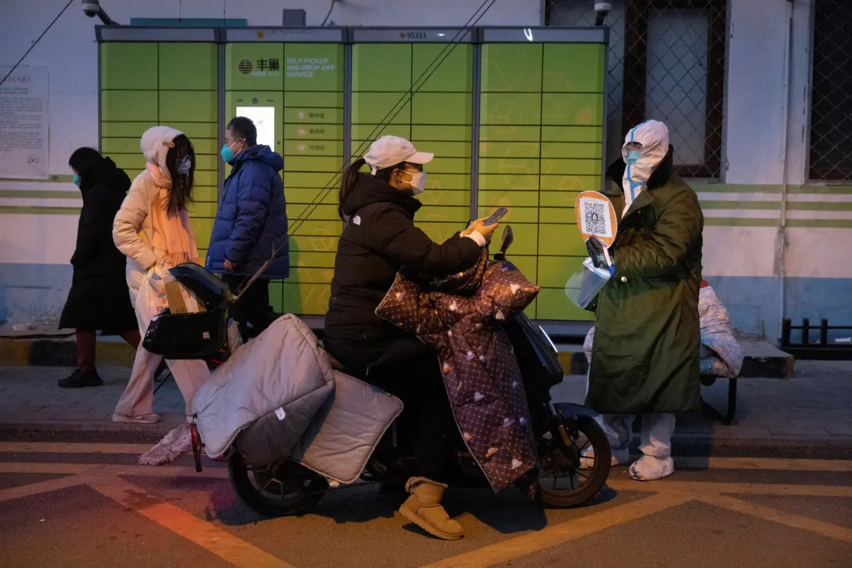 A woman presents her health code to a pandemic prevention worker in a protective suit to enter a residential compound as coronavirus disease (COVID-19) outbreaks continue in Beijing