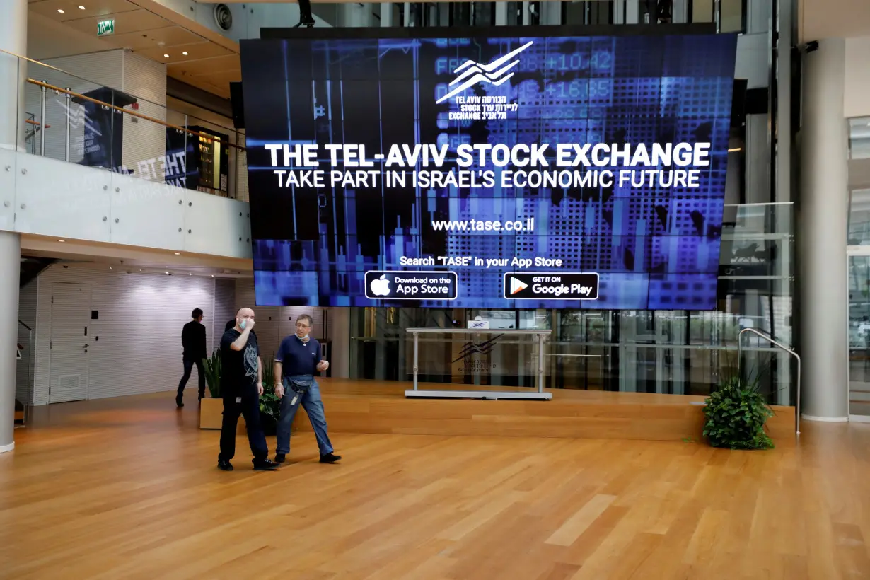 FILE PHOTO: Men walk past an electronic board at the Tel Aviv Stock Exchange, in Tel Aviv