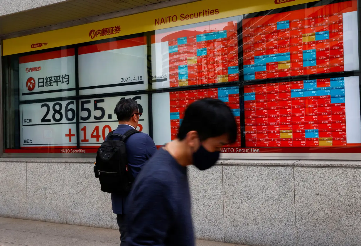 Passersby walk past an electric board displaying Japan's Nikkei share average outside a brokerage in Tokyo