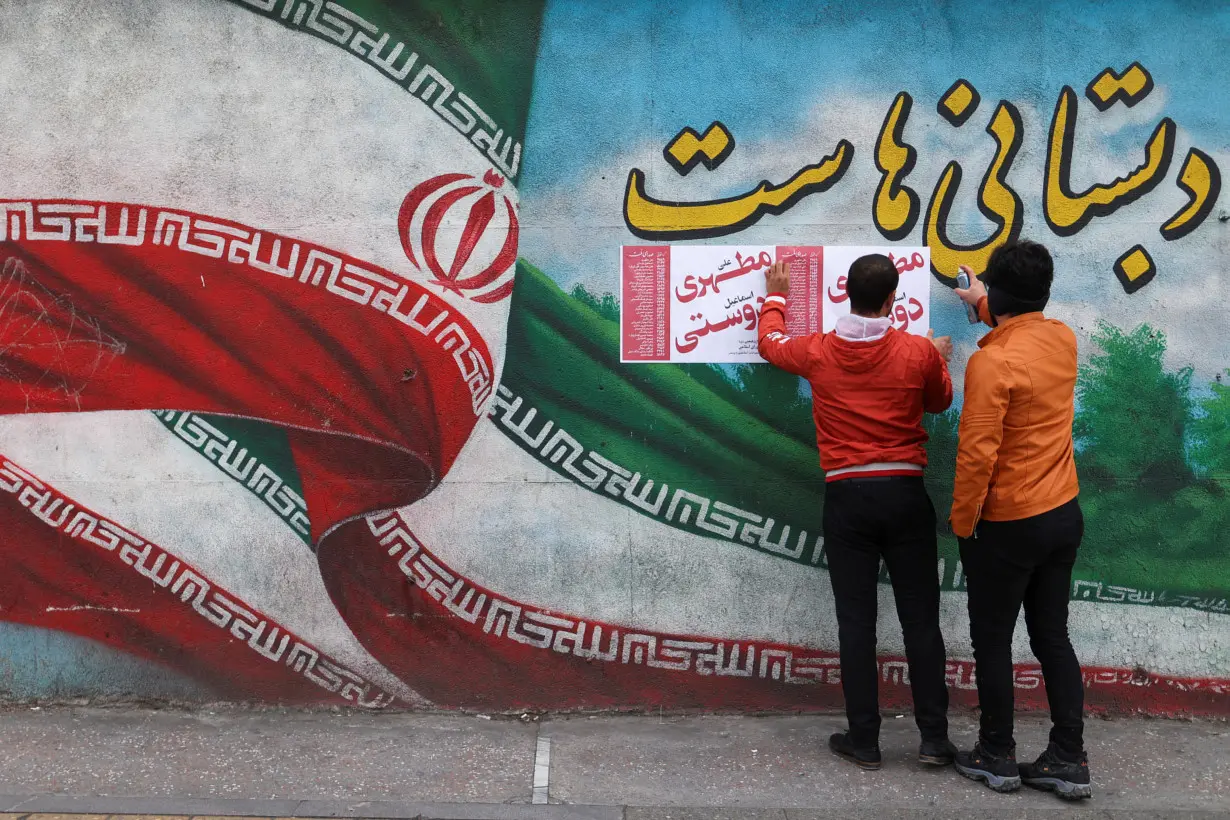 Iranian men put campaign posters on a wall during the last day of election campaigning in Tehran