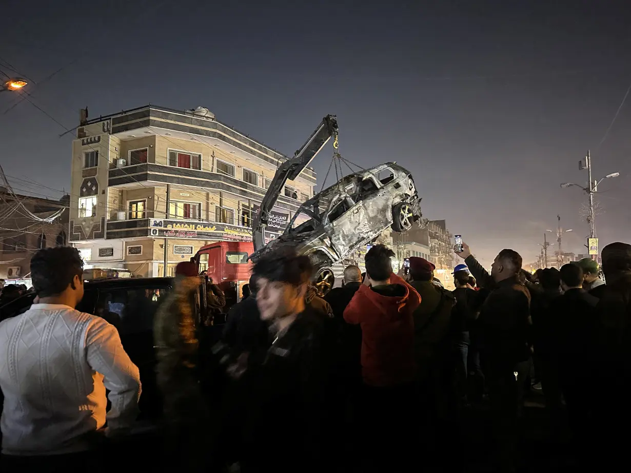 People gather as a destroyed vehicle is loaded onto a truck, after a deadly drone strike in Baghdad