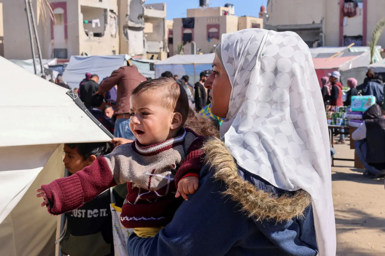 A displaced Palestinian woman holds her son as she waits to get him examined by a doctor, outside a medical tent, in Rafah in the southern Gaza Strip