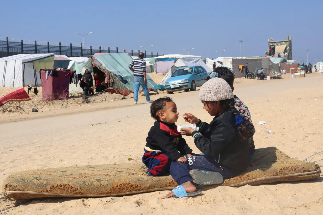 Displaced Palestinian girl feeds her brother, in Rafah