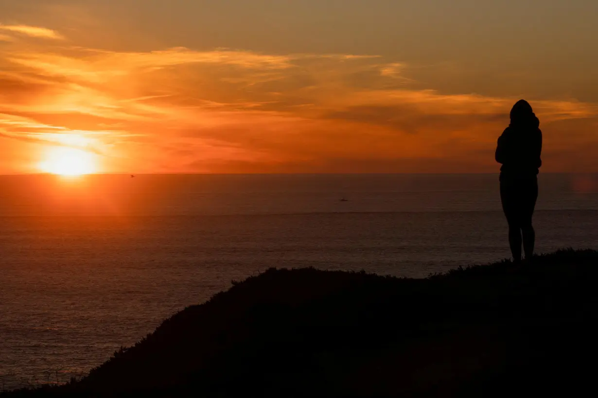 FILE PHOTO: A woman watches the sunset over the Pacific Ocean along Highway 1 near Half Moon Bay