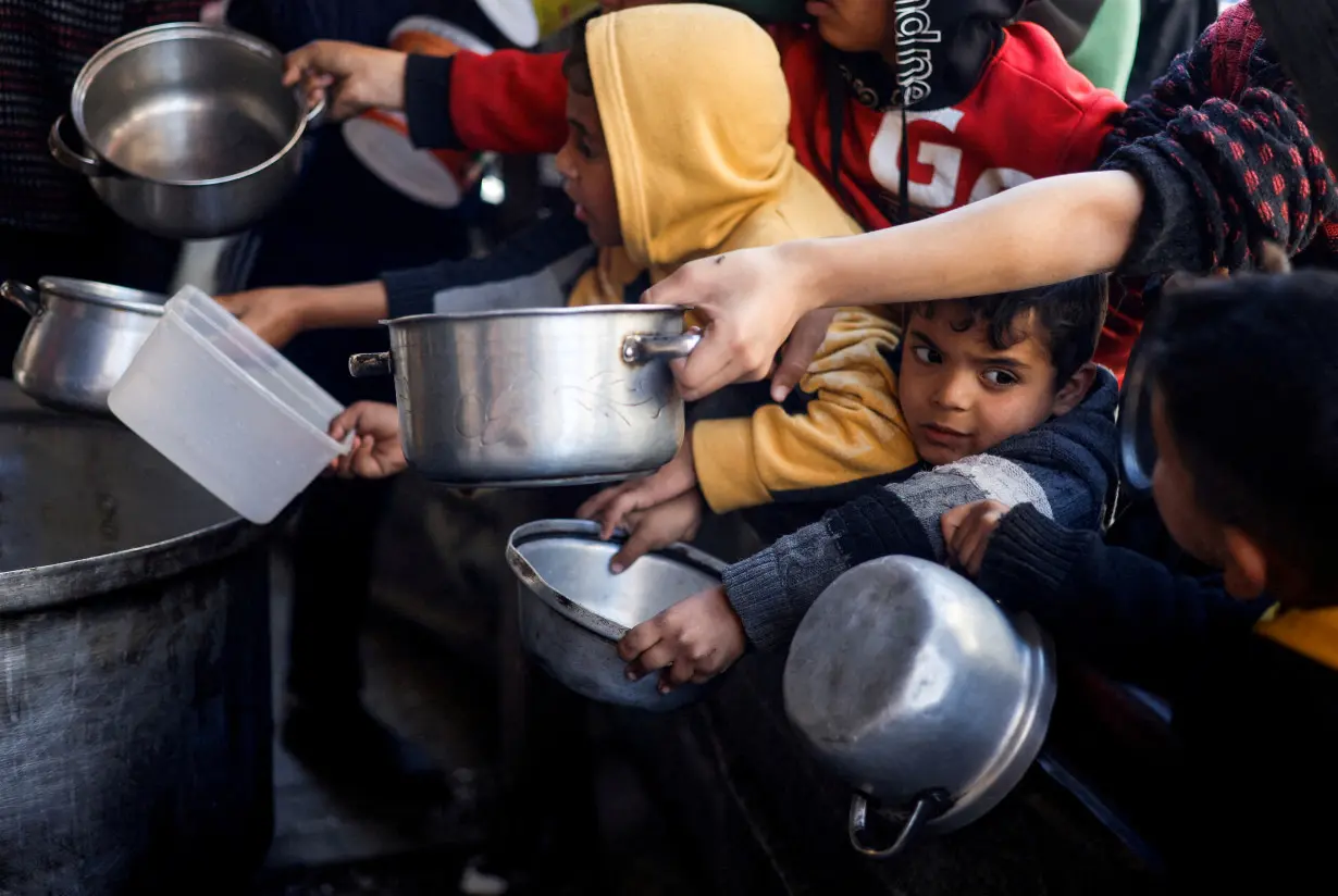 FILE PHOTO: Palestinian children wait to receive food cooked by a charity kitchen amid shortages of food supplies, in Rafah