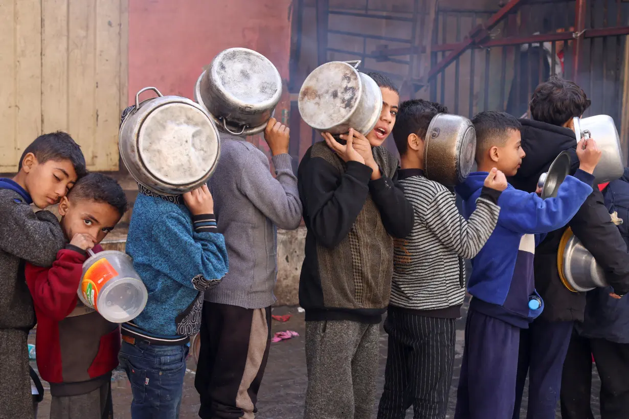 Palestinian children carry pots as they queue to receive food cooked by a charity kitchen, in Rafah in the southern Gaza Strip