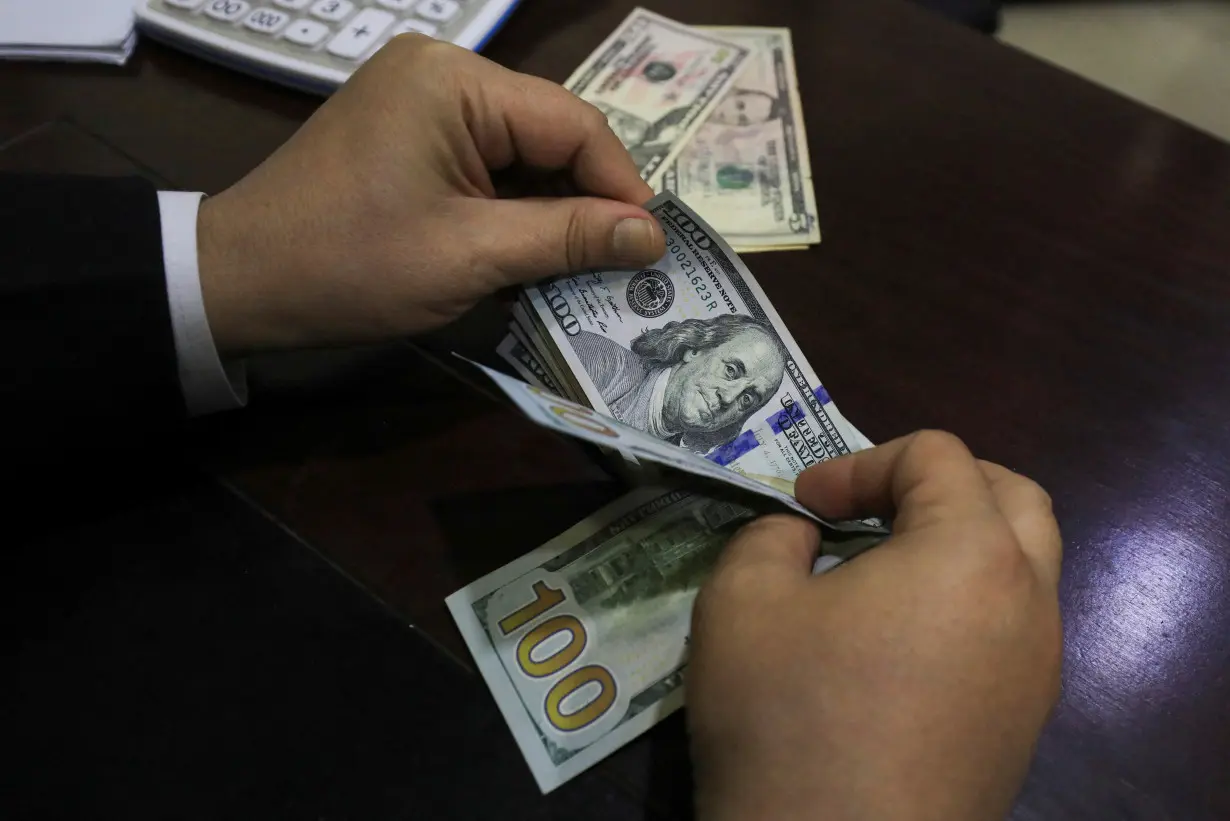 A trader counts U.S. dollar banknotes at a currency exchange booth in Peshawar