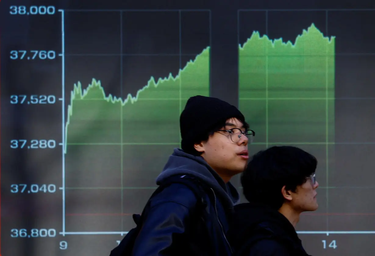 Passersby walk past an electric screen displaying a graph showing Japan's Nikkei share average movements outside a brokerage in Tokyo