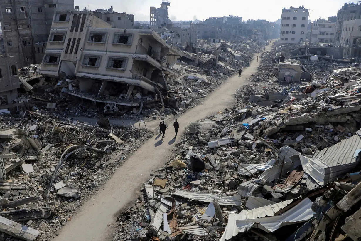 FILE PHOTO: Palestinians walk past destroyed houses, in Jabalia refugee camp