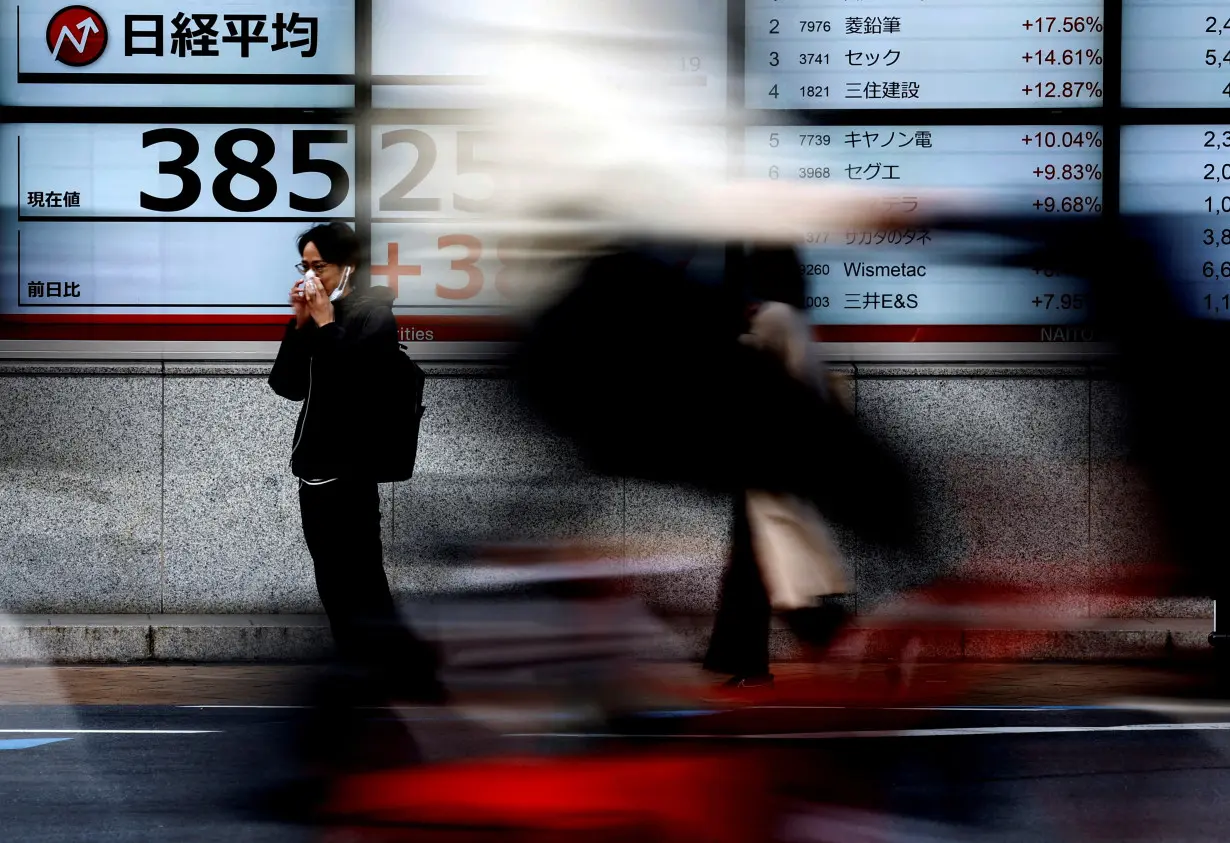 Passersby walk past electronic screens displaying Japan's Nikkei share average outside a brokerage in Tokyo