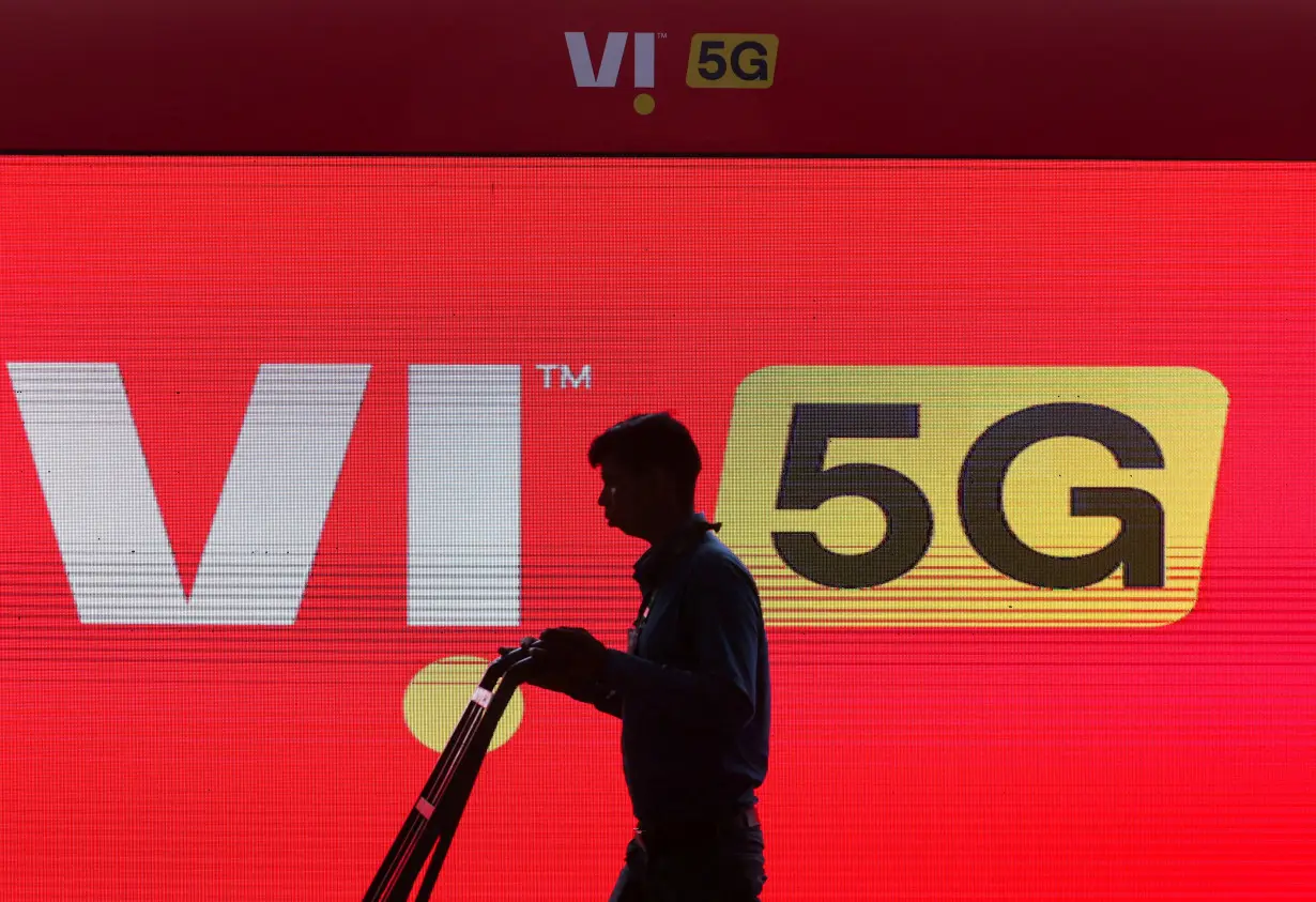 FILE PHOTO: A man walks across the LED display board showing the logo of Vodafone-Idea at the ongoing India Mobile Congress 2022, at Pragati Maidan, in New Delhi