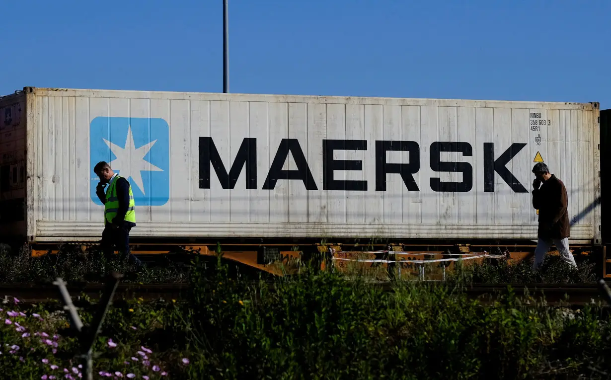 FILE PHOTO: Workers talk on their mobile phones as a Maersk container is transported by a train near a port of Barcelona