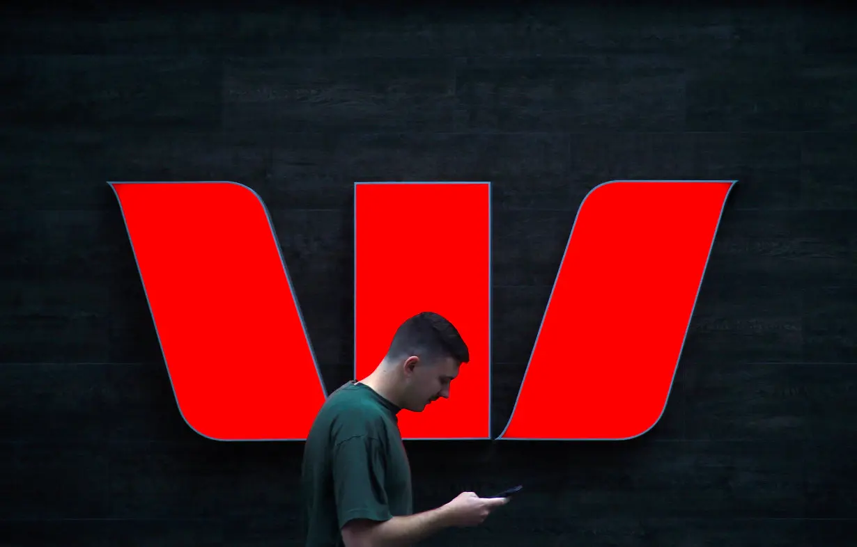 A pedestrian looks at his phone as he walks past a logo for Australia's Westpac Banking Corp located outside a branch in central Sydney