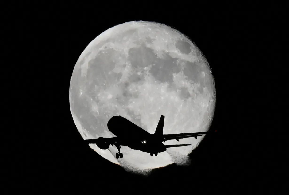 FILE PHOTO: Aircraft passes in front of moon near Heathrow Airport in London