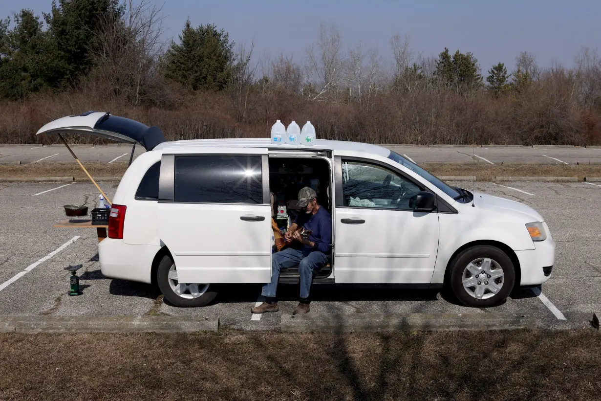 Jim Brown, who lives full time in his van, plays a broken guitar while enjoying the sun at Sessions Lake, in Ionia, Michigan,