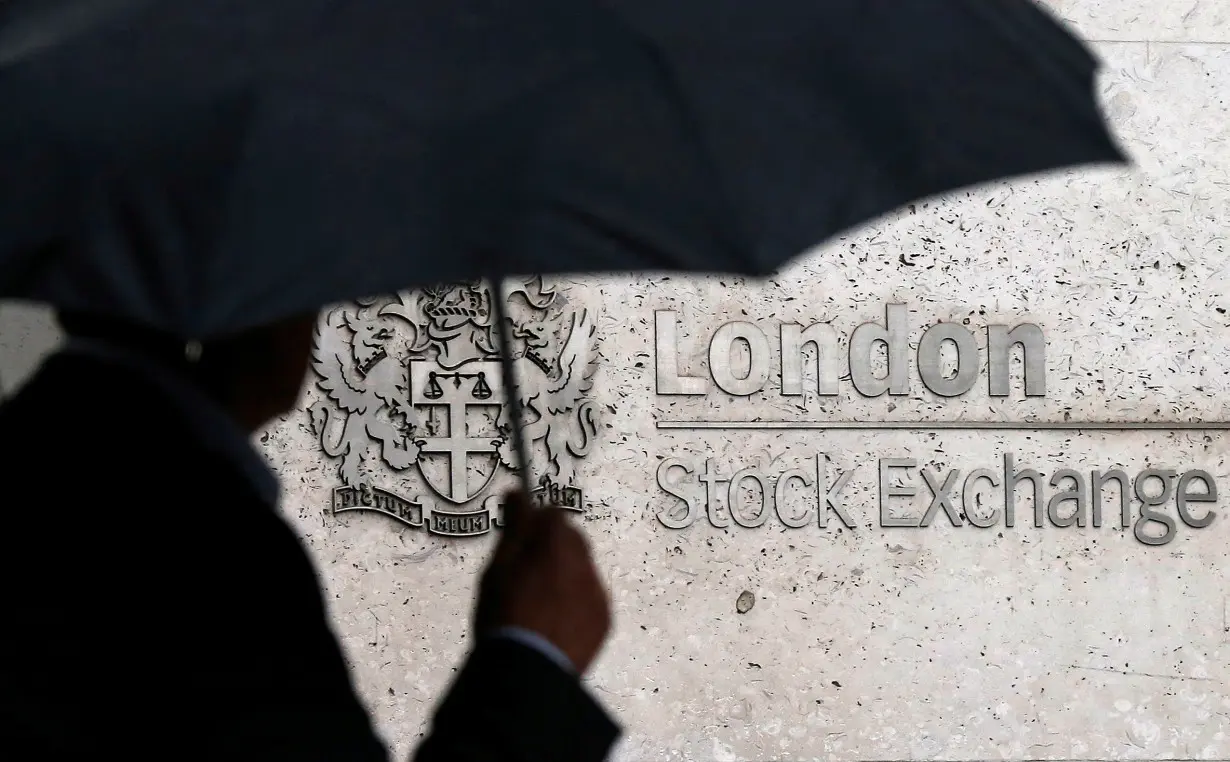 FILE PHOTO: A man shelters under an umbrella as he walks past the London Stock Exchange