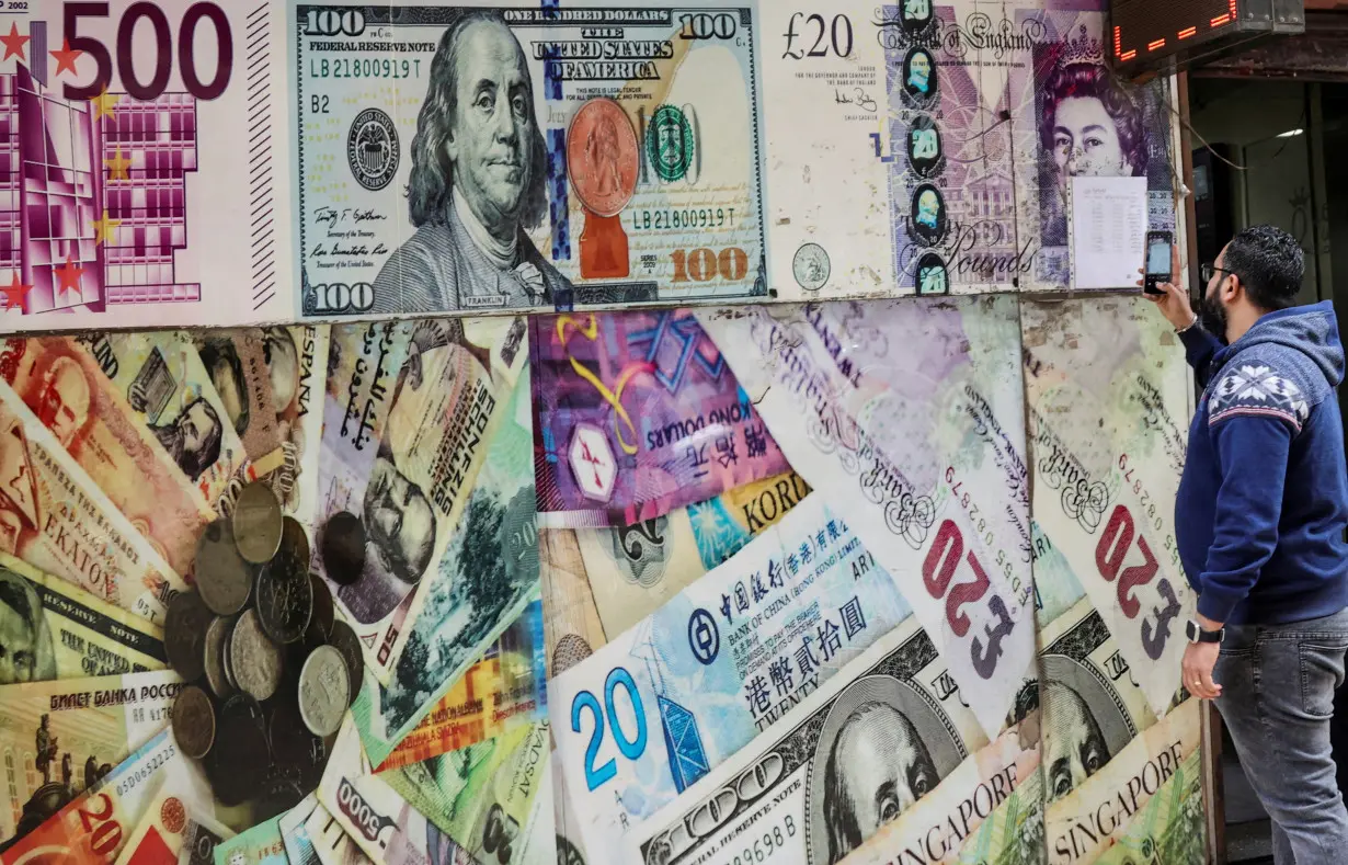 FILE PHOTO: A man takes a photograph of exchange rates in front of an exchange point, displaying images of different currencies, in Cairo