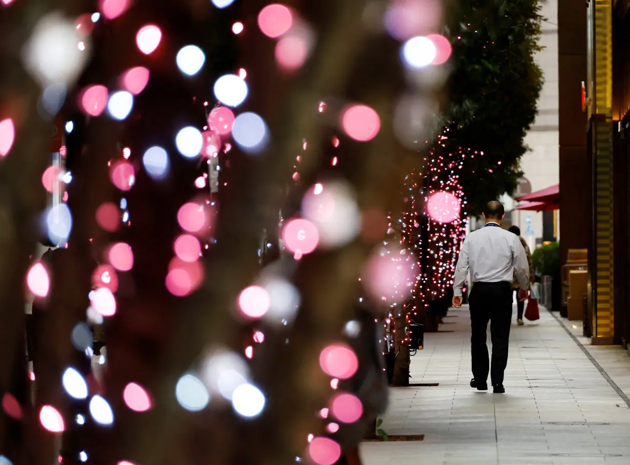 An office worker walks past illuminated trees at a business district in Tokyo