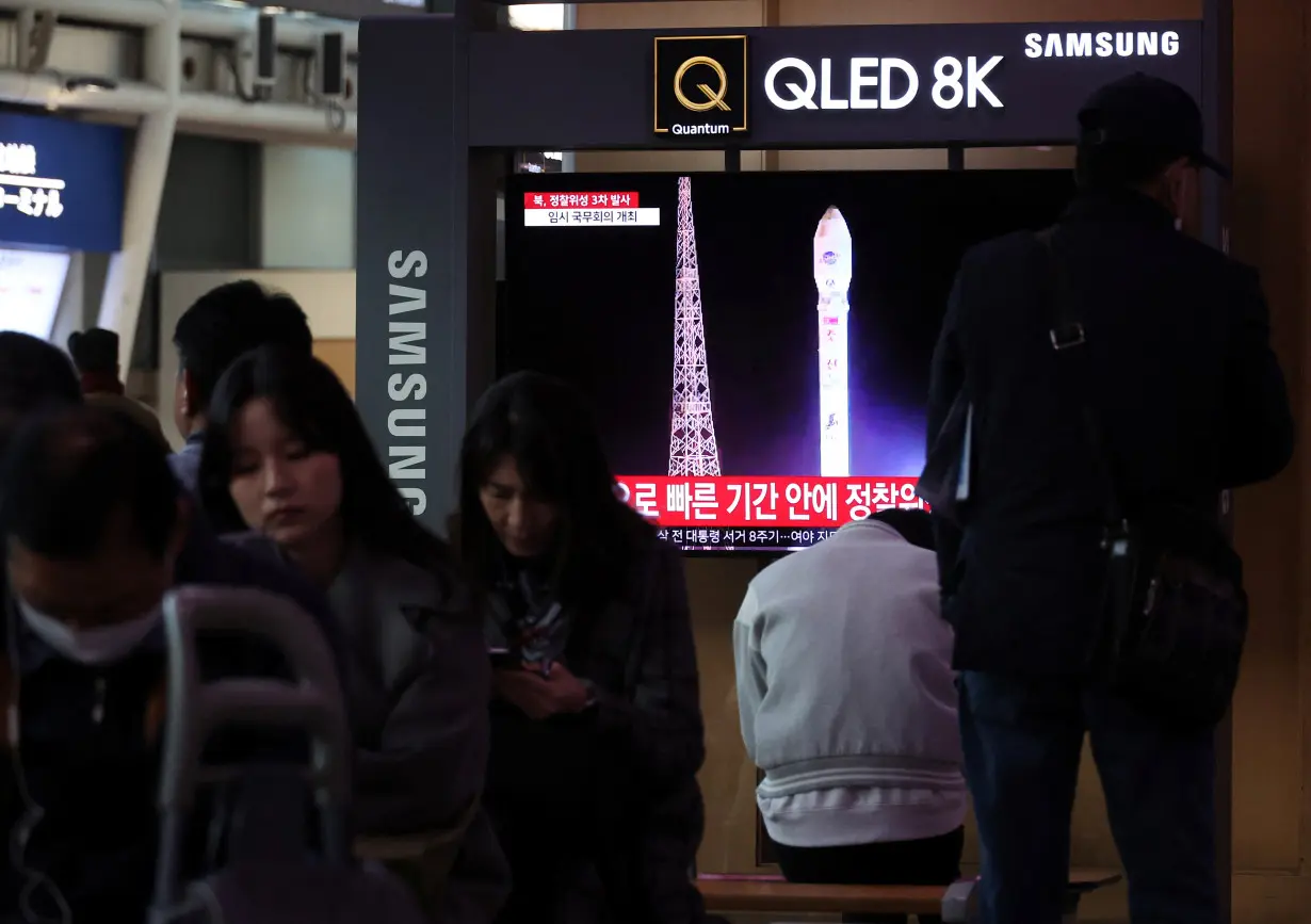 People sit by a TV broadcasting a news report on North Korea launching a military satellite, at a railway station in Seoul