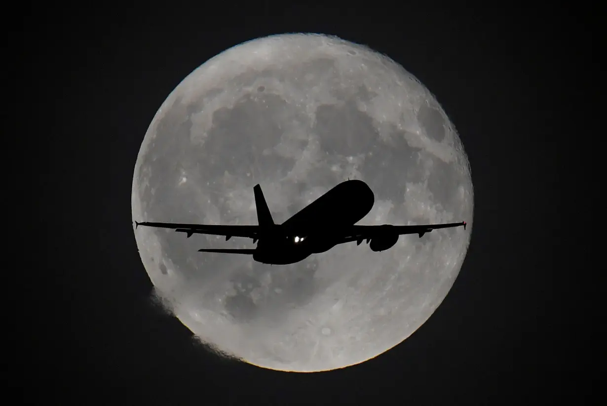 Passenger plane is seen with the moon behind as it begins its final landing approach to Heathrow Airport in London