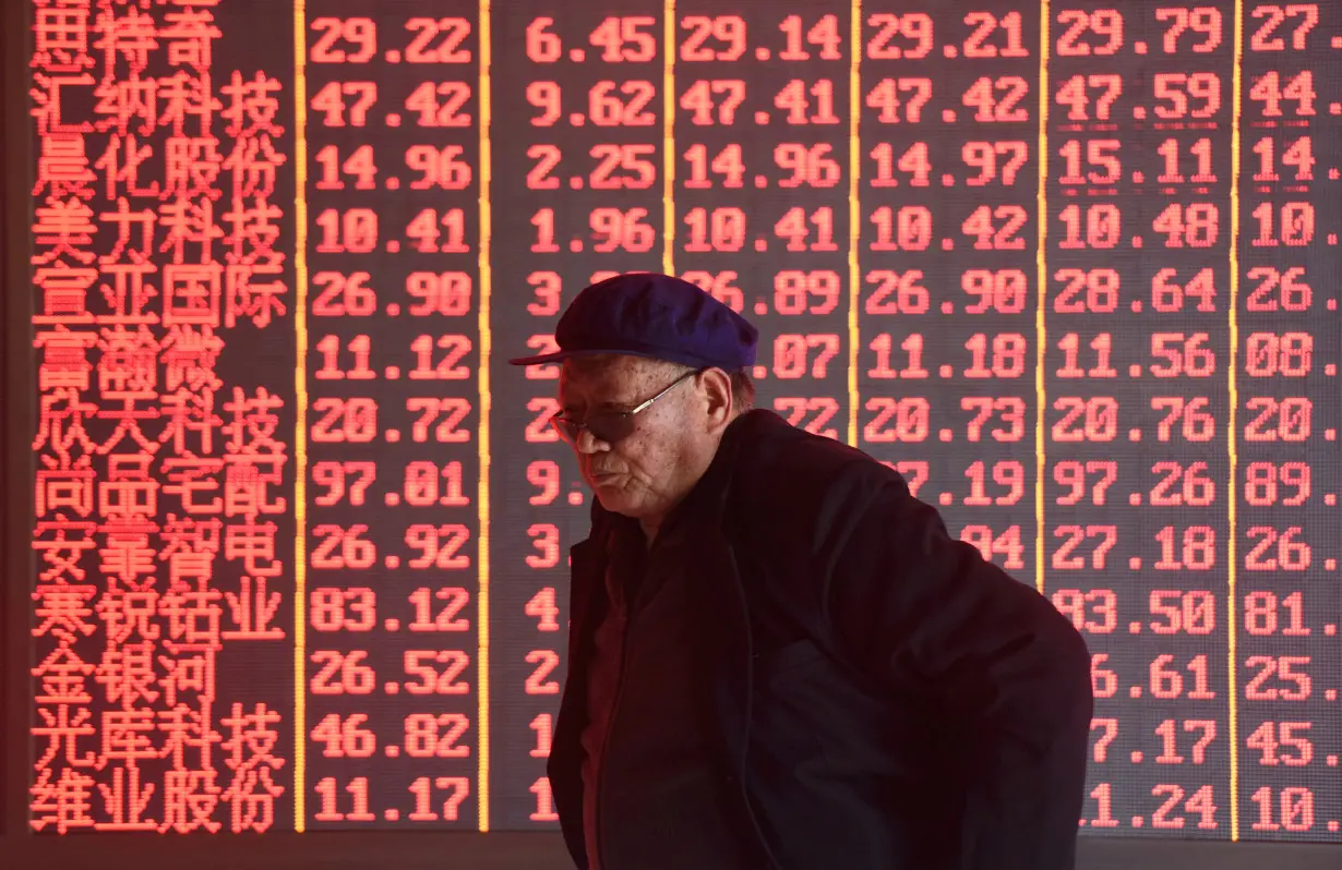 FILE PHOTO: Man stands in front of an electronic board displaying stock information at a brokerage firm in Hangzhou