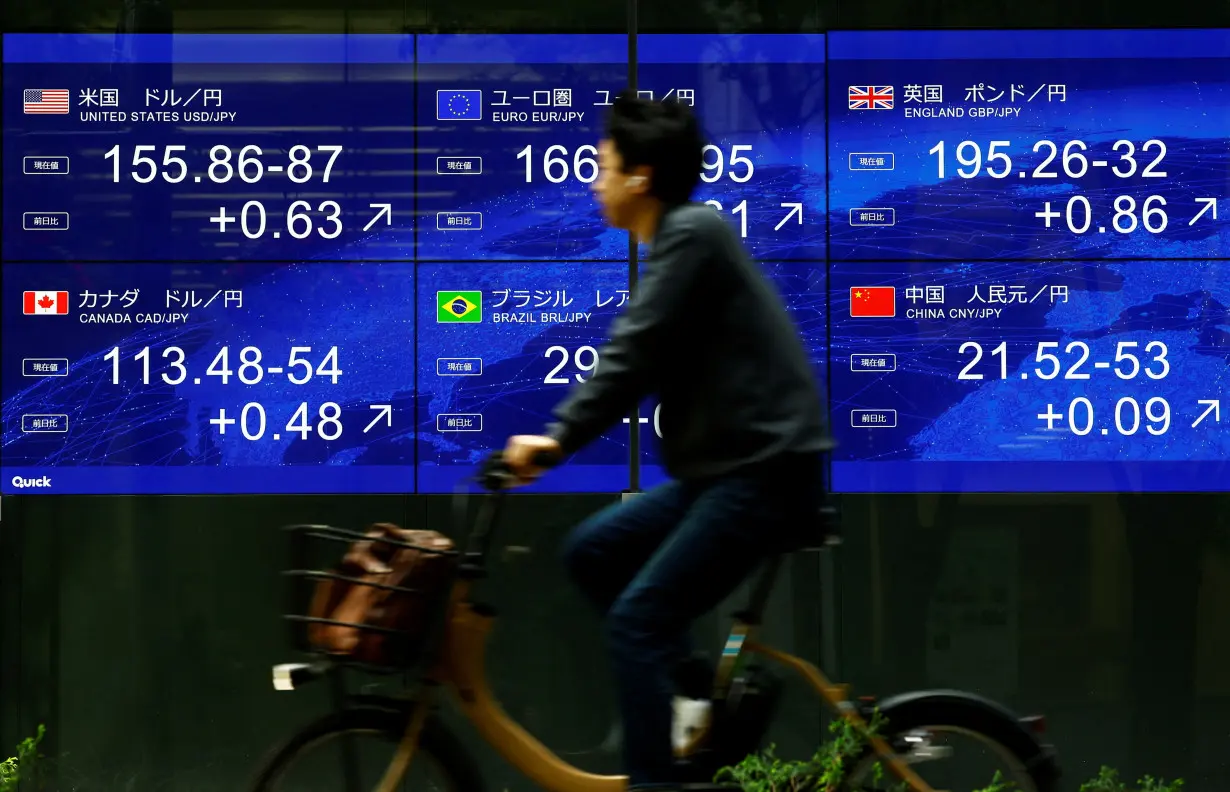 FILE PHOTO: A man rides a bicycle past an electronic screen displaying the current Japanese Yen exchange rate against the U.S. dollar and other foreign currencies in Tokyo