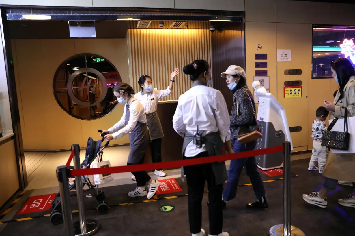 Staff members attend customers at the entrance of a Haidilao hotpot restaurant in Beijing