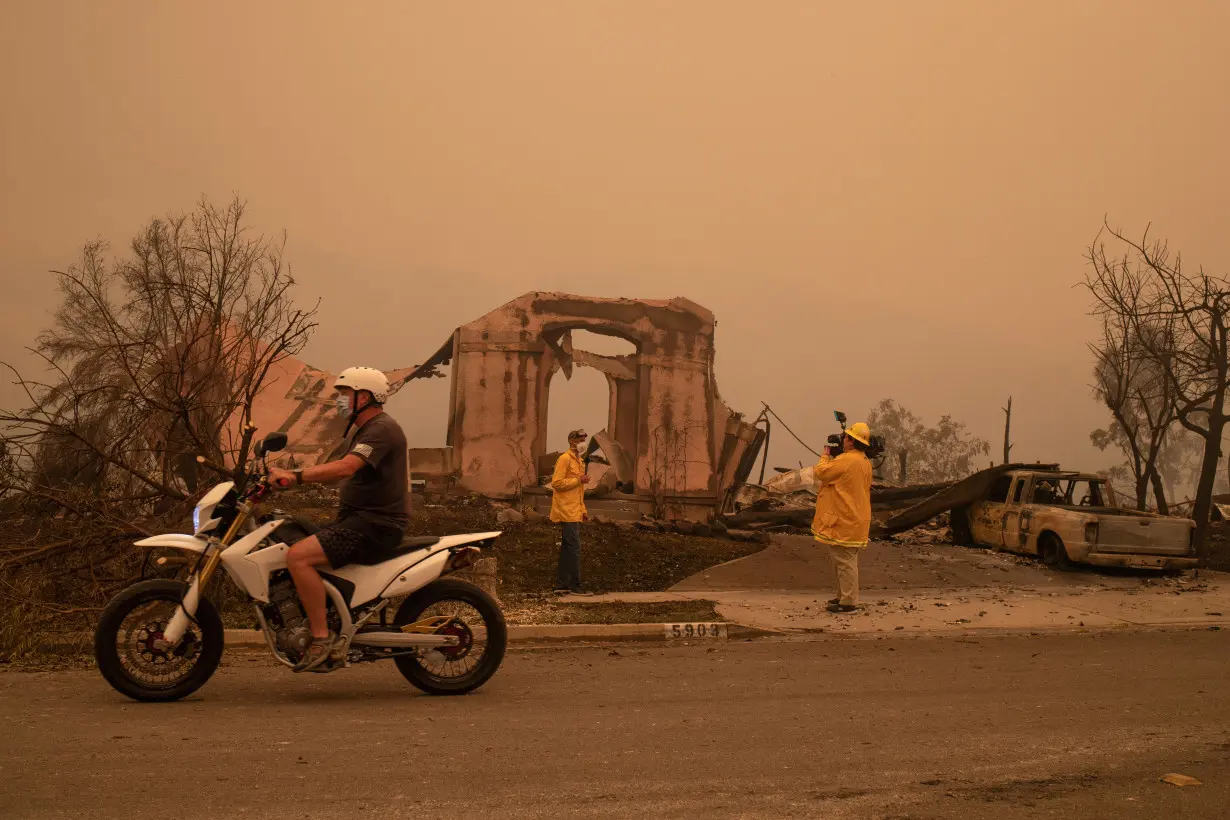 FILE PHOTO: A man rides past journalists reporting on the aftermath of the Shady Fire after it advanced into the Skyhawk neighborhood of Santa Rosa