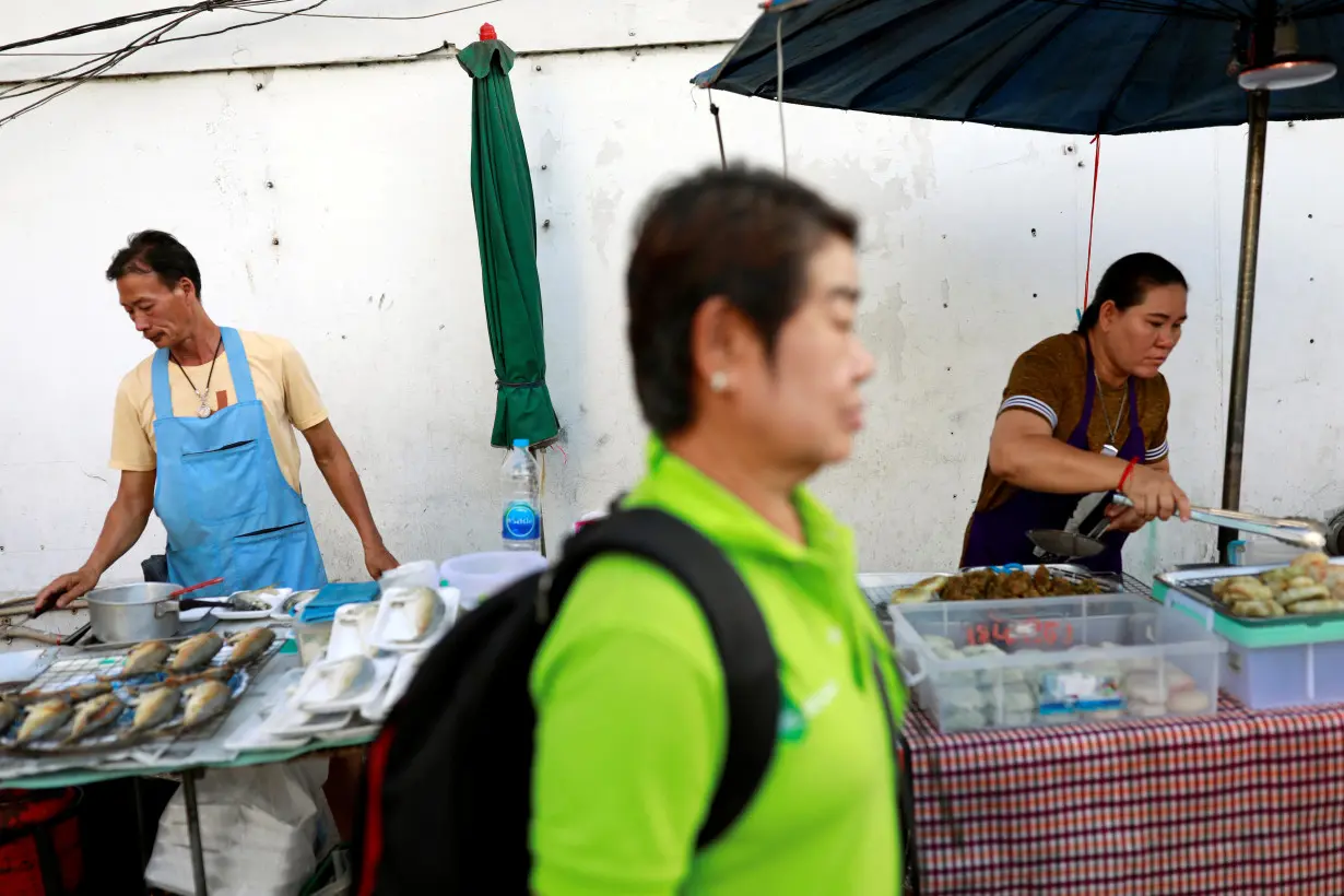 A person walks pass some vendors on the street at a market in Bangkok