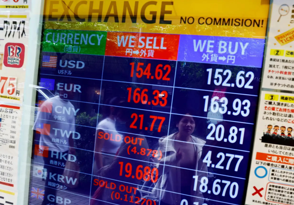 People are reflected on an electric screen displaying Japanese Yen exchange rates against the U.S. dollar and other foreign currencies at a currency exchange shop in Tokyo