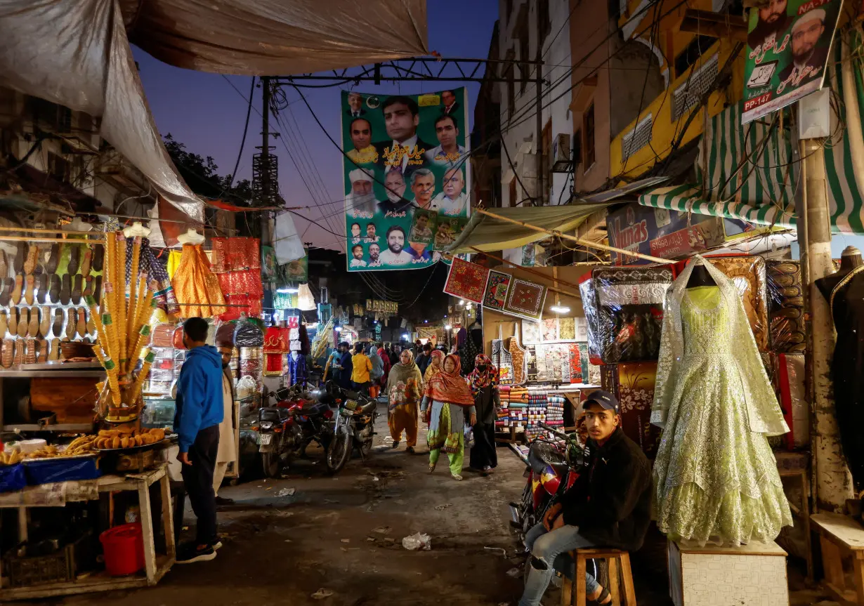 FILE PHOTO: People walk past a campaign banner of political party, ahead of the general elections, at the market of Walled City in Lahore