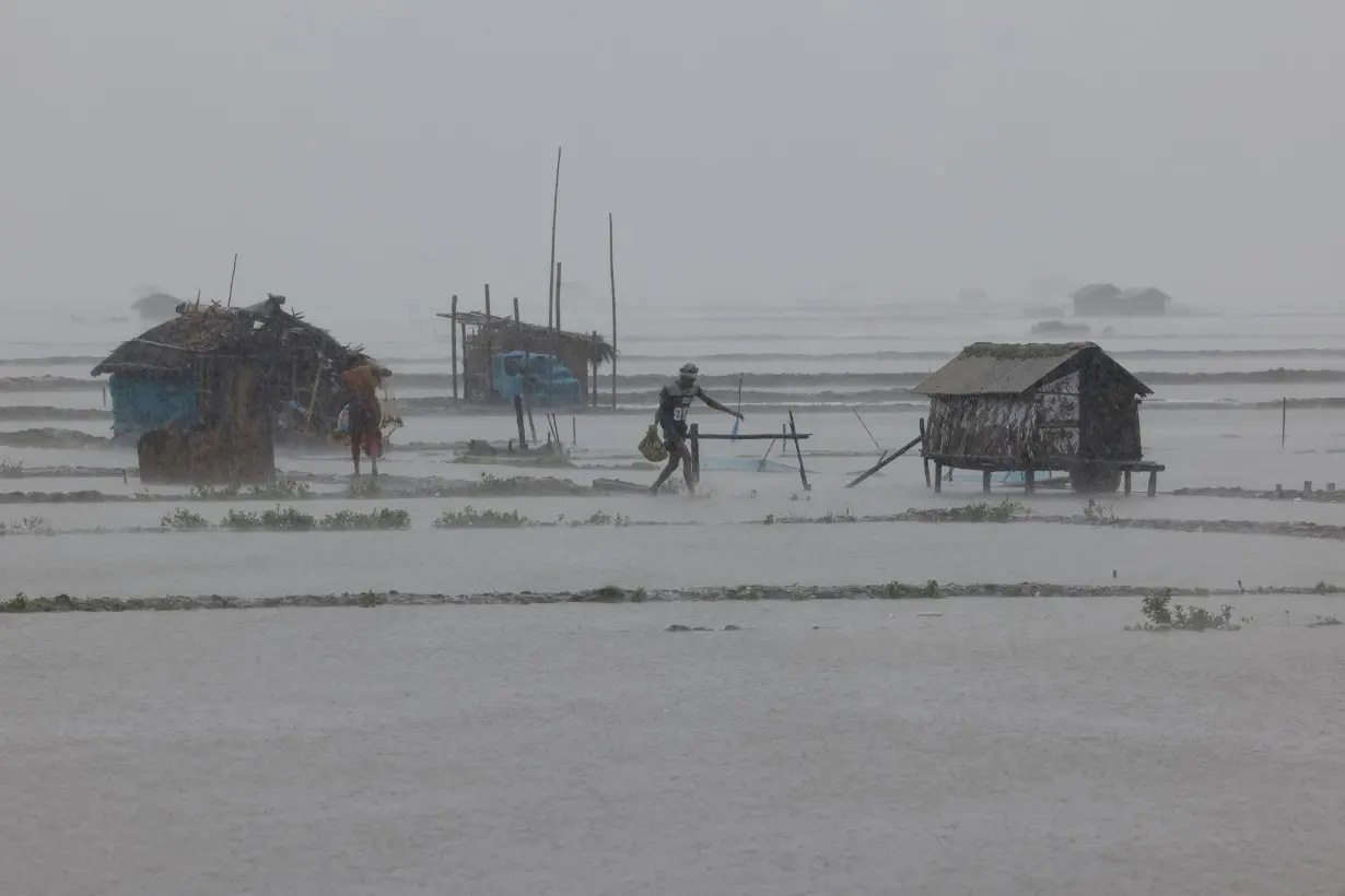 People walk along flooded shrimp and crab farms due to heavy rain as Cyclone Remal passes the country in the Shyamnagar area of Satkhira