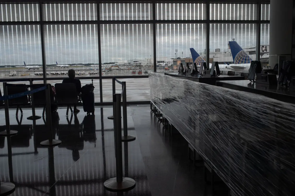 United Airlines planes are seen in background as a lone traveler awaits next to a closed restaurant at IAH airport in Houston