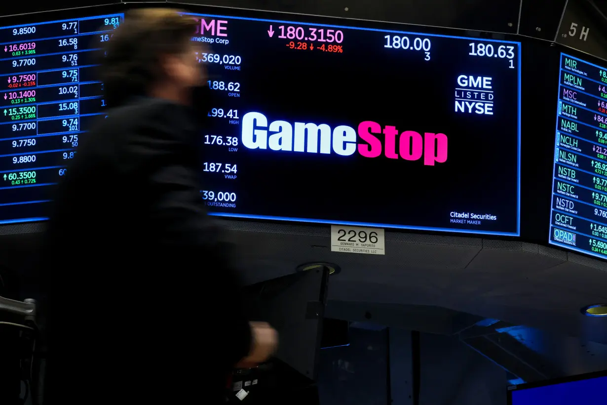 A screen displays the logo and trading information for GameStop at the NYSE in New York