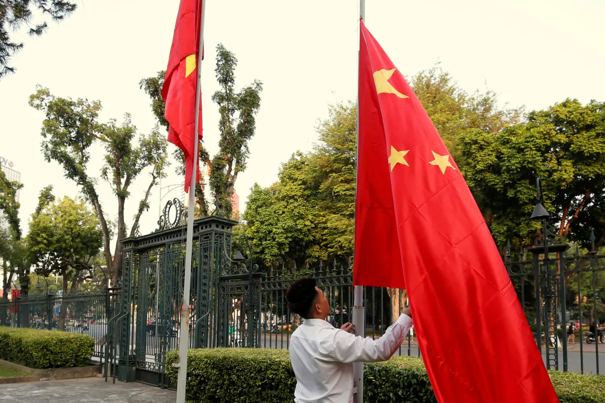 A man raises a Chinese flag next to a Vietnamese flag before a meeting between China's FM Wang and Vietnam's DPM and FM Minh at the Government Office in Hanoi