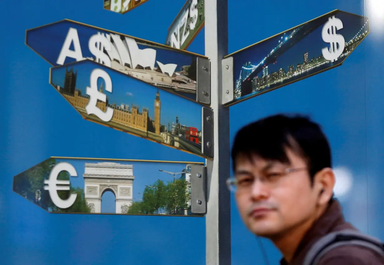 FILE PHOTO: A man walks past various currency signs outside a brokerage in Tokyo