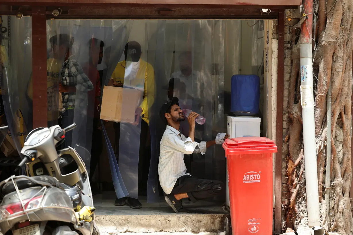 Delivery partner with Blinkit, an Indian online-delivery company, drinks water outside one of the company's dark stores on a hot summer day during a heatwave in New Delhi