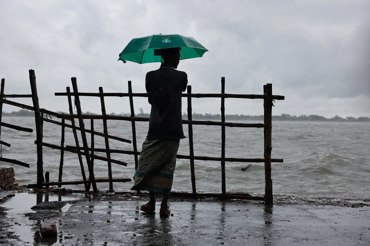 A man stands on the bank of Kholpetua river with an umbrella before the Cyclone Remal hits the country in the Shyamnagar area of Satkhira