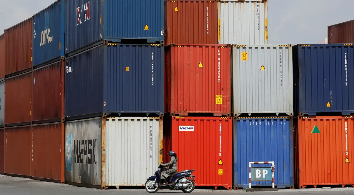 Woman rides a motorcycle as she passes containers at Hai Phong port