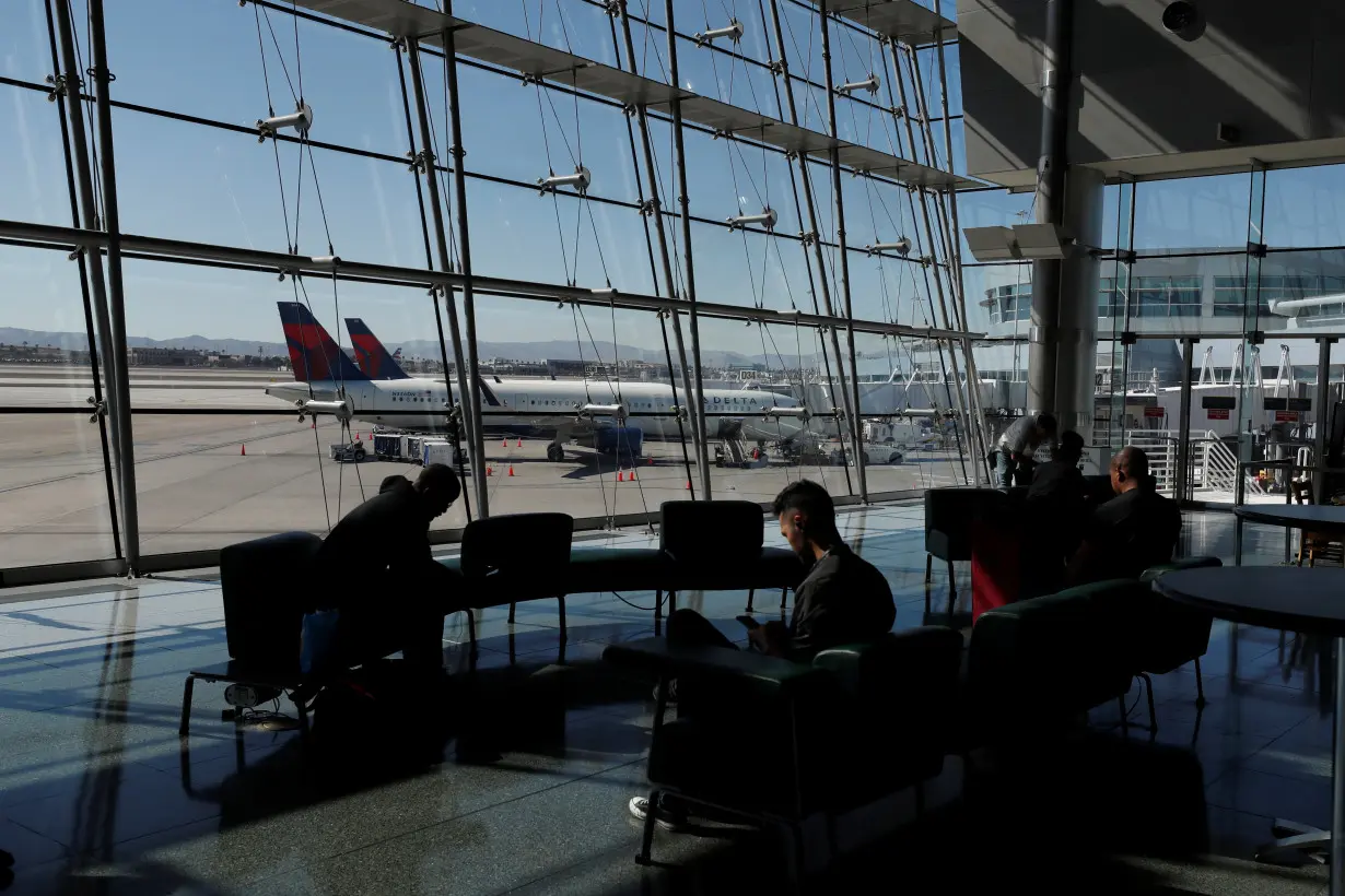 FILE PHOTO: Travelers sit in a lounge area as Delta Air Lines plane park at a gate in McCarran International Airport in Las Vegas