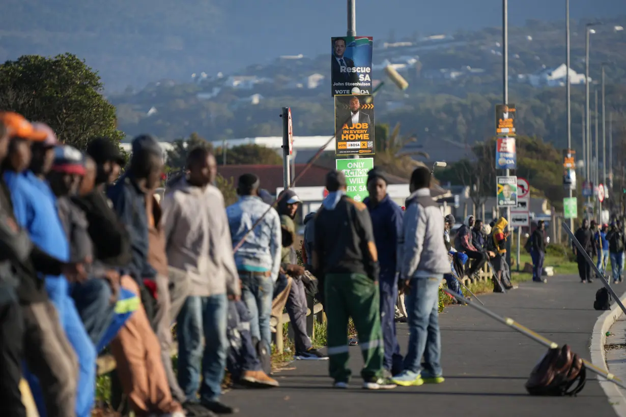 Job seekers sit beneath campaign posters for the South African general elections, in Cape Town