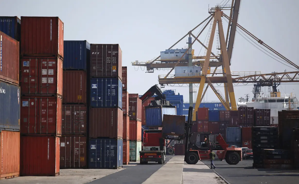 Workers unload containers using a forklift at a port in Lisbon