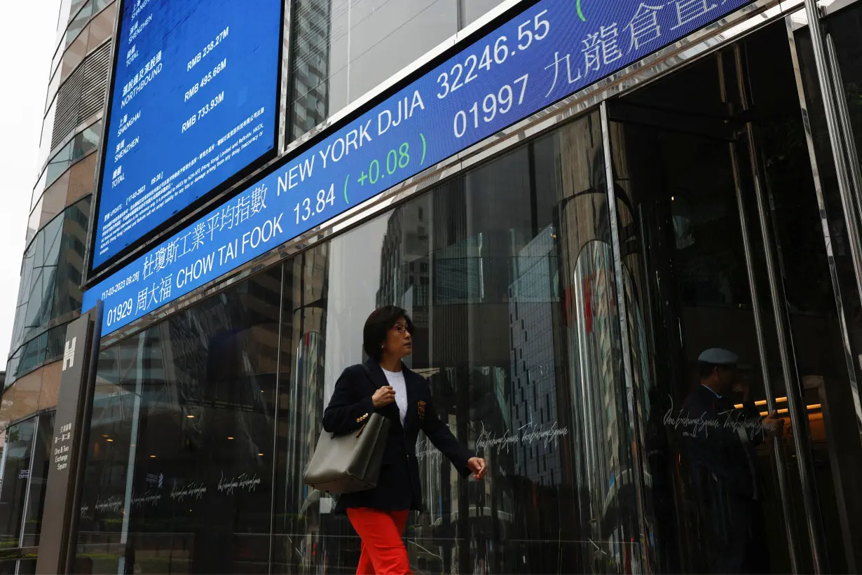 A woman walks past a screen displaying the Hang Seng Index at Central district, in Hong Kong