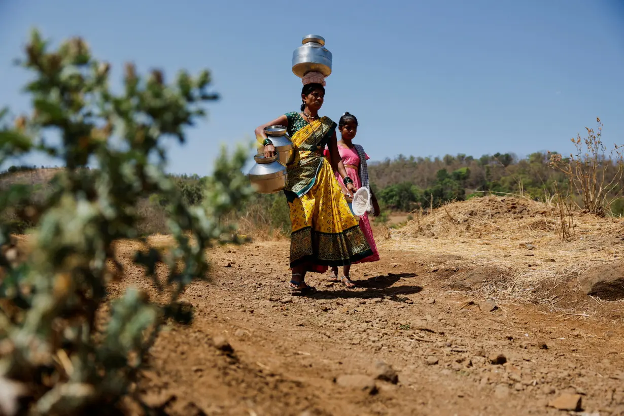 People carrying pots walk towards a well to draw water from it on a hot day in Kasara