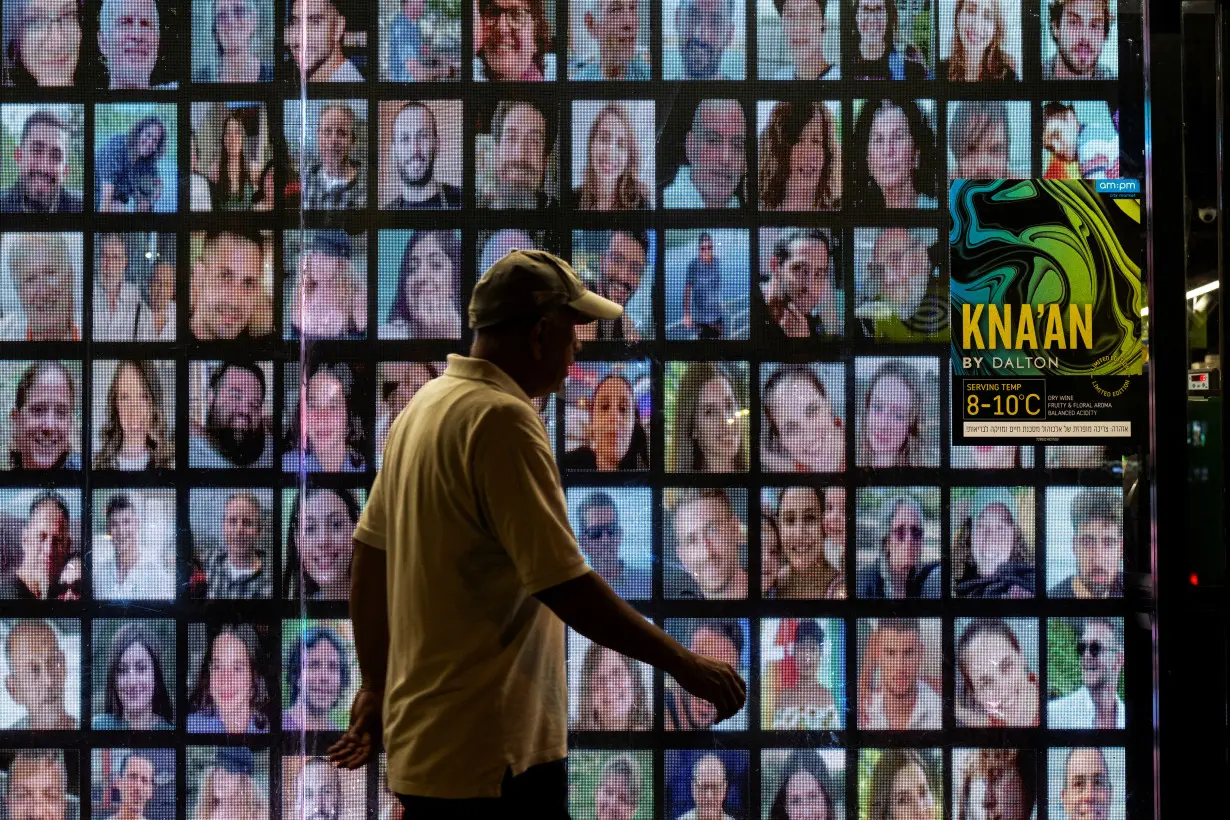 A person walks past pictures of hostages kidnapped during the deadly October 7 attack by Hamas, projected on a screen, in Tel Aviv