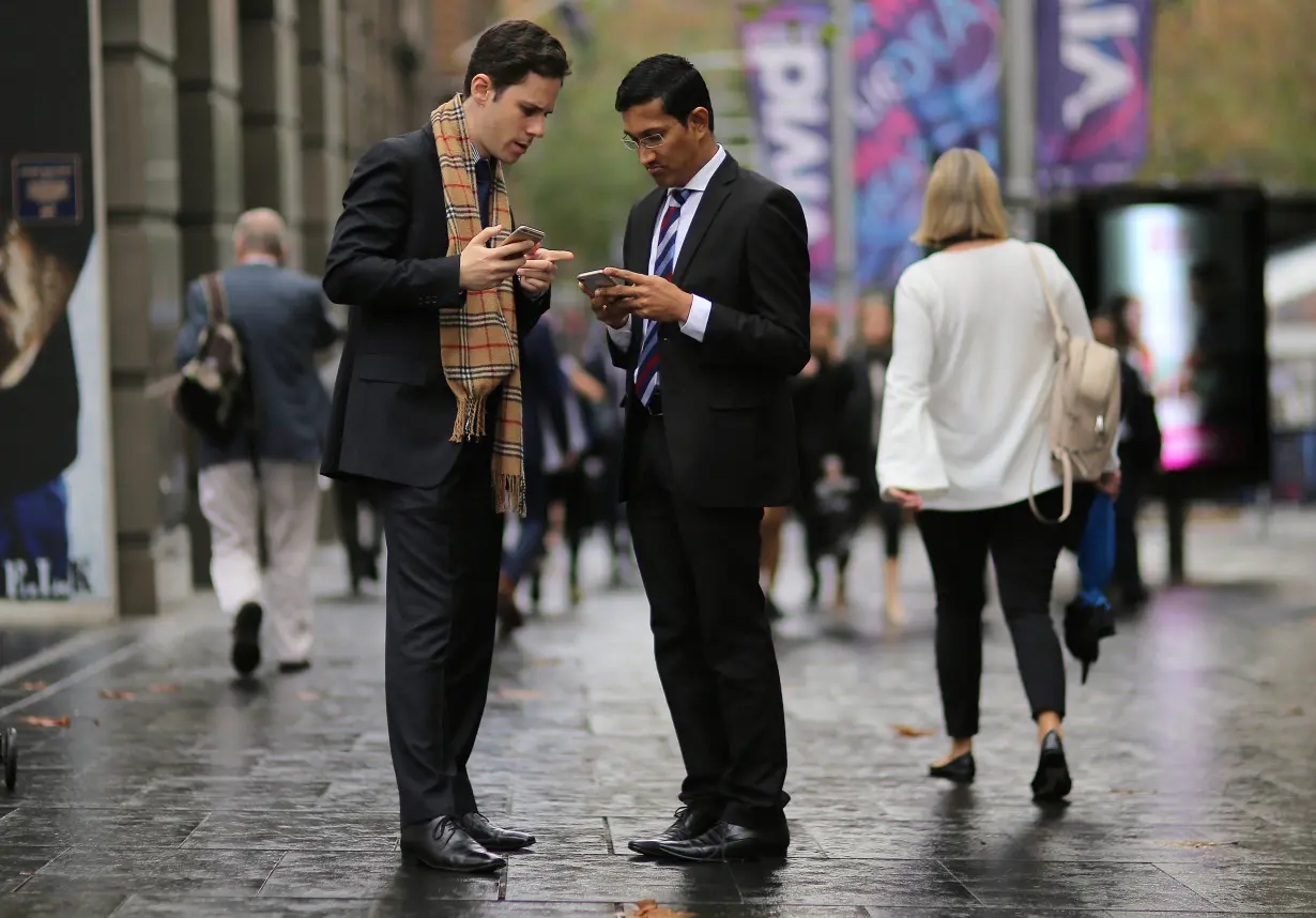 Businessmen use their phones as they stand in the central business district (CBD) of Sydney in Australia