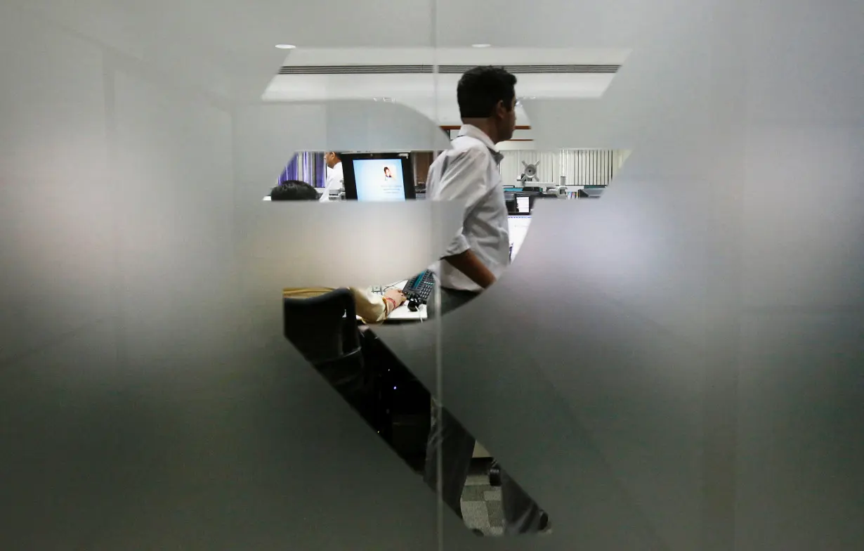 FILE PHOTO: FILE PHOTO: A currency trader is pictured through the symbol for the Indian Rupee on the floor of a trading firm in Mumbai