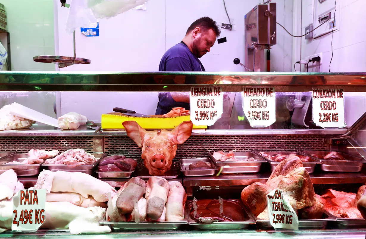 A butcher handles pork pieces at a market stall in Madrid